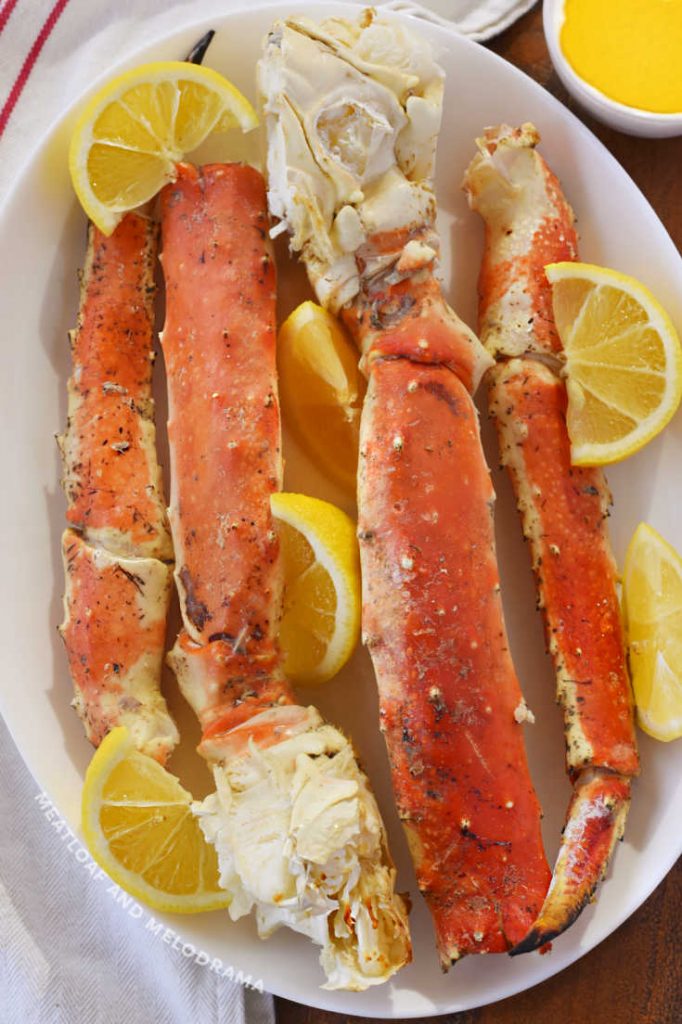 grilled king crab legs  on a white platter with lemon wedges