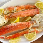 grilled king crab legs on a white platter with lemon wedges and melted butter