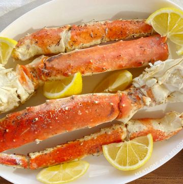 grilled king crab legs on a white platter with lemon wedges and melted butter