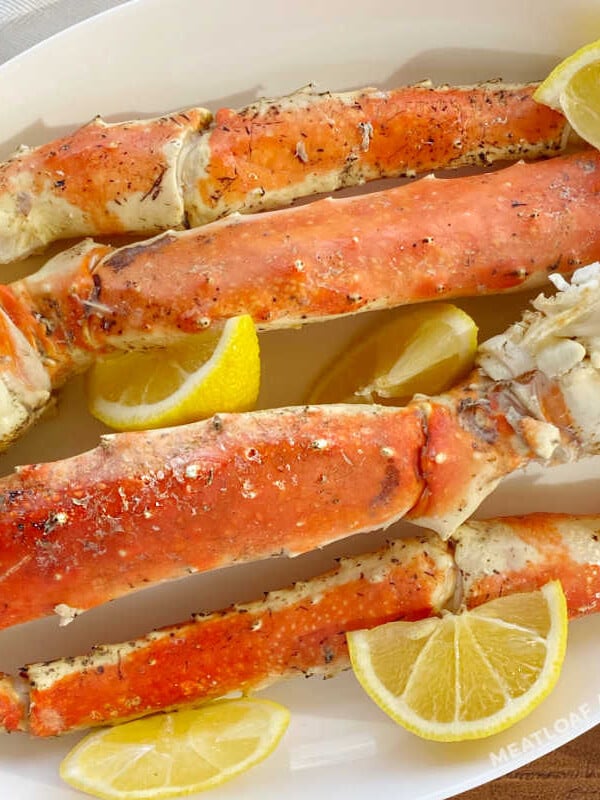 grilled king crab legs on a white platter with lemon wedges and melted butter