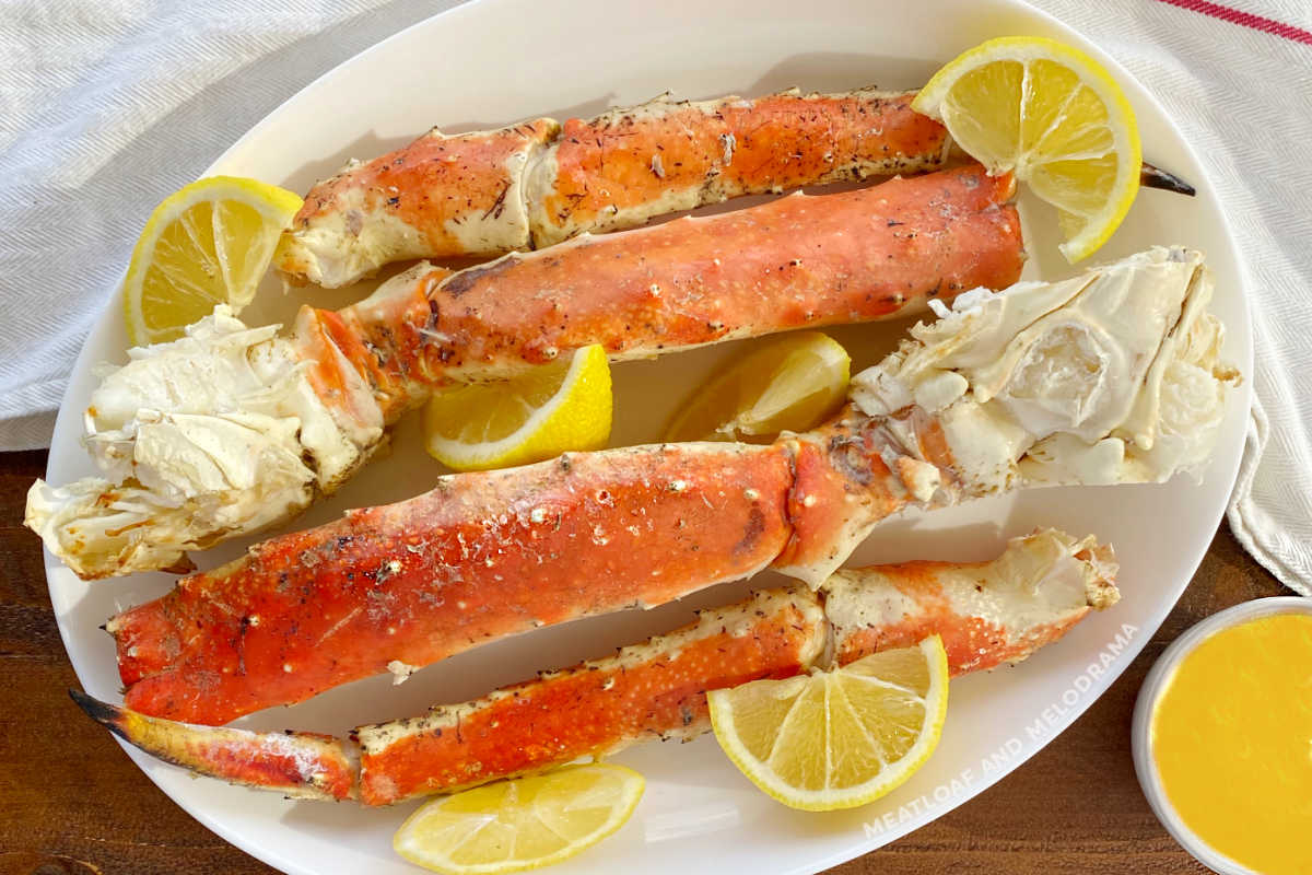 grilled king crab legs on a white platter with lemon slices and melted butter