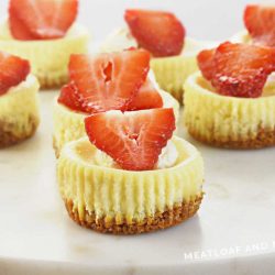 baked mini cheesecakes topped with strawberry slices and whipped cream on marble cake stand