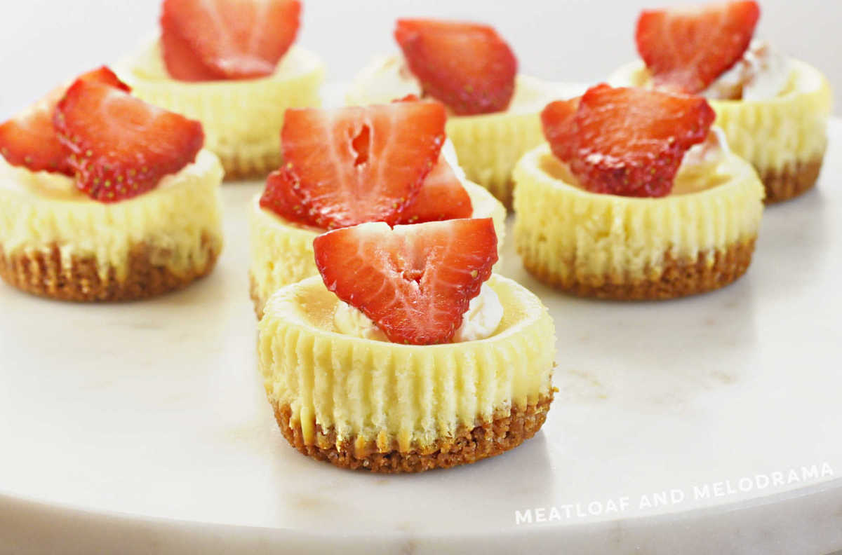 mini cheesecakes with graham cracker crust topped with fresh strawberries on marble cake stand