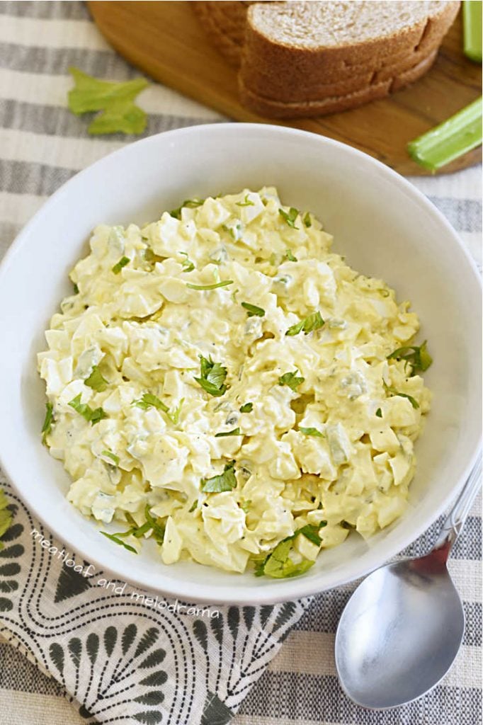 egg salad topped with celery leaves in a white serving bowl