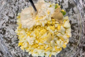 chopped hard boiled eggs and celery with mayo and mustard in mixing bowl