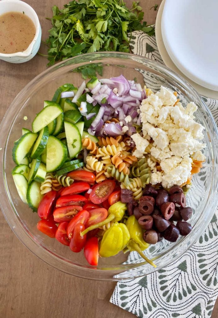 pasta salad ingredients with kalamata olives, feta, cucumbers, tomatoes, onions, peppers and rotini