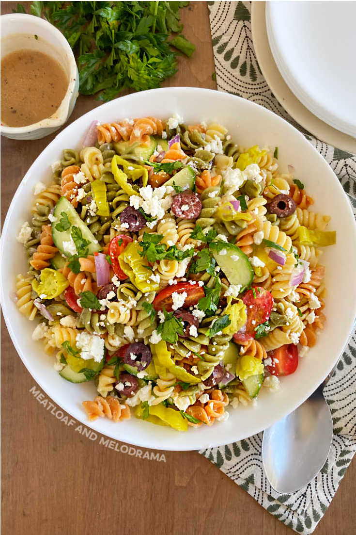 overhead shot of greek pasta salad with tri color pasta in white serving bowl on table