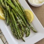microwave asparagus on white platter with lemon slices and parmesan cheese