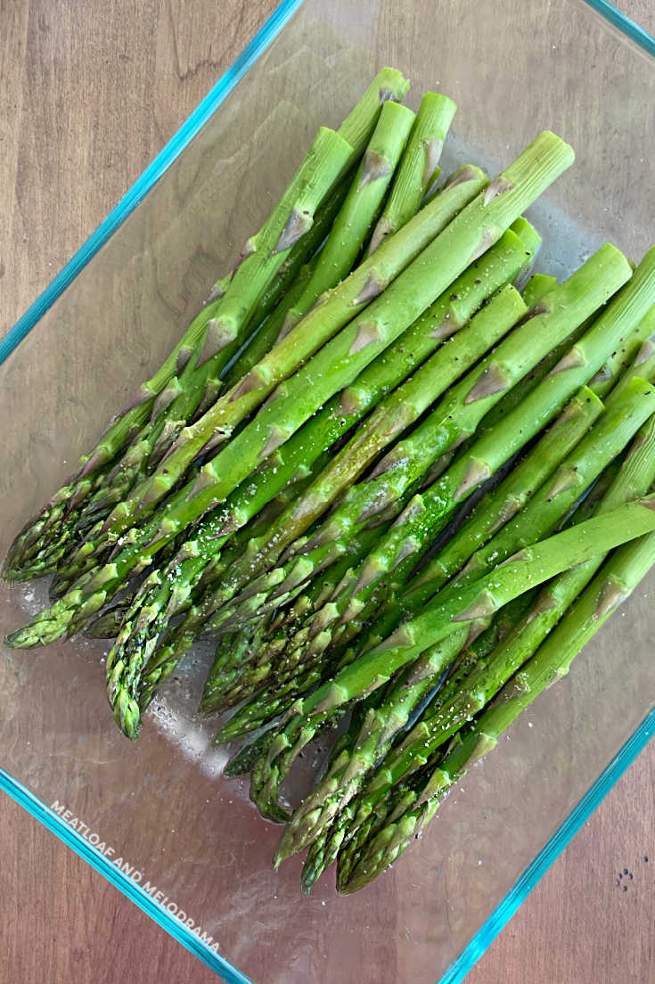 fresh asparagus with water, salt, pepper and garlic powder in glass dish
