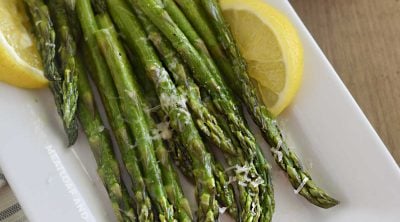 microwave asparagus on white platter with lemon slices and parmesan cheese
