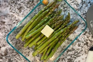 raw asparagus with butter in glass baking dish