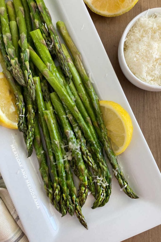 microwave asparagus on a white platter with lemon slices and parmesan cheese