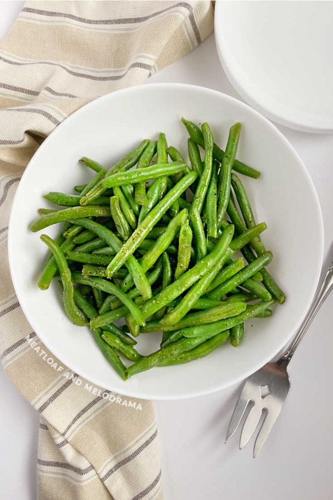 steamed green beans in white serving dish with fork