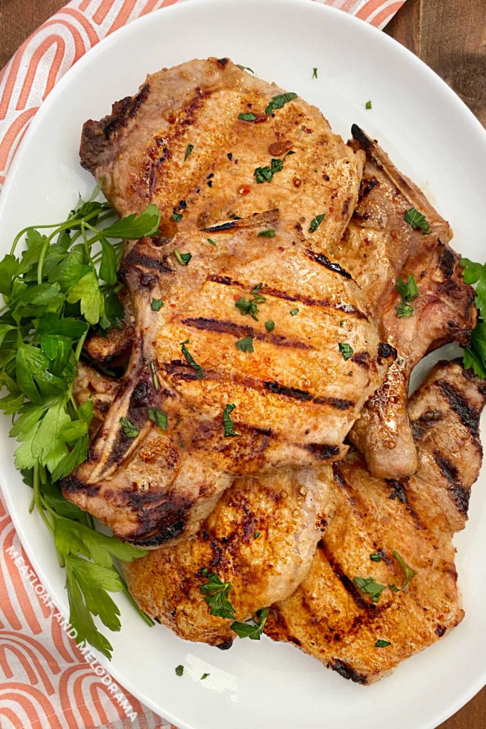 grilled pork chops on a white platter with parsley