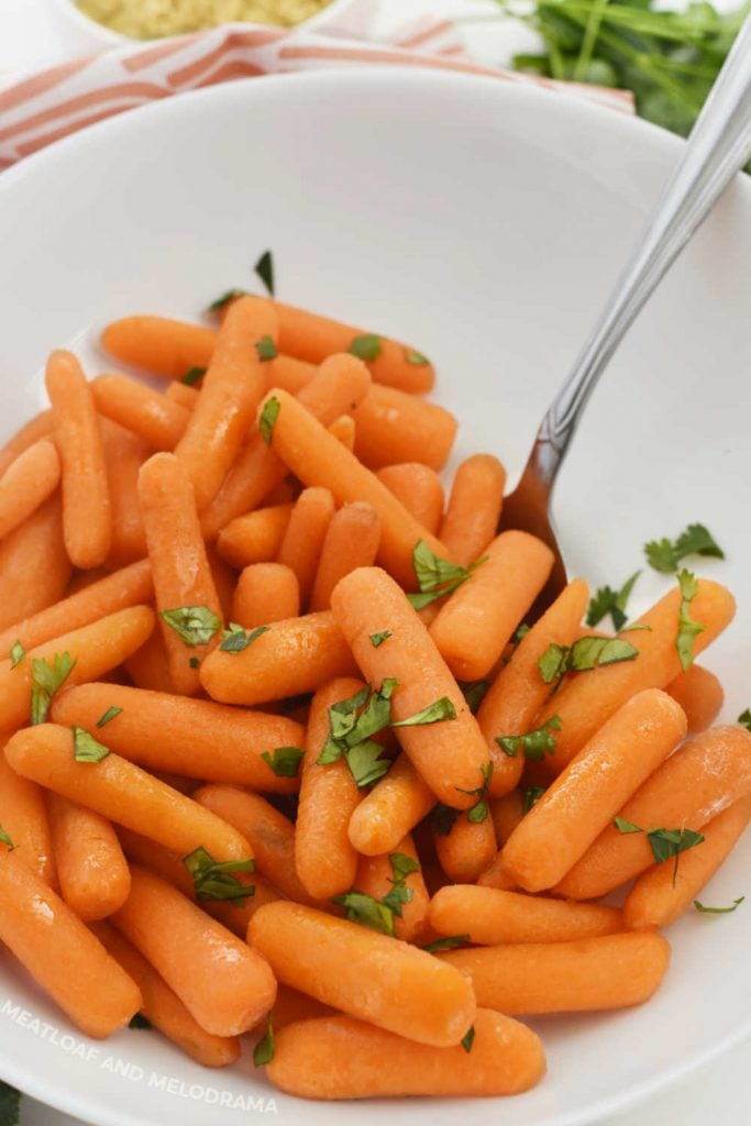 carrots with butter and brown sugar in a white serving bowl with parsley