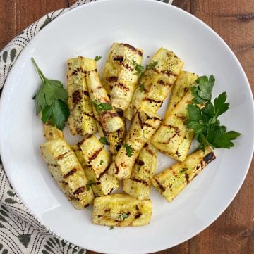 grilled yellow squash spears with parsley on a white platter
