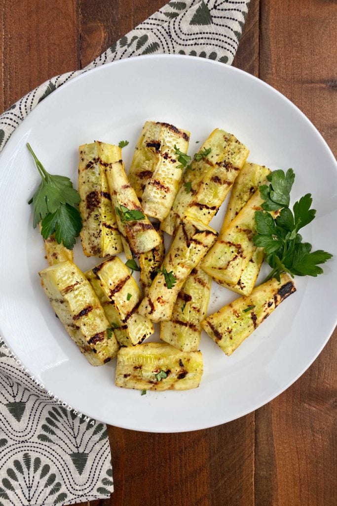 grilled yellow summer squash on a white platter with parsley