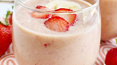 strawberry banana protein smoothie with peanut powder in a glass with fruit on the table