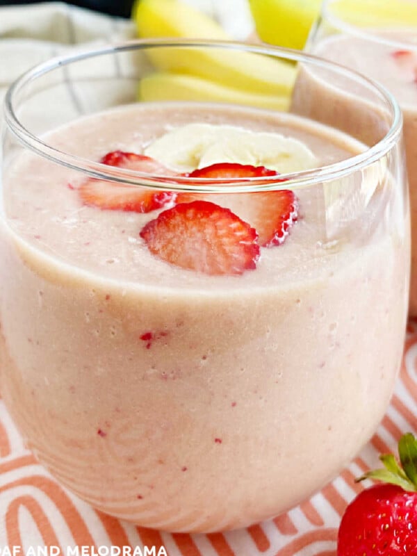 strawberry banana protein smoothie with peanut powder in a glass with fruit on the table
