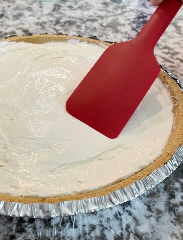 smooth kool aid pie filling in graham cracker crust with red spatula