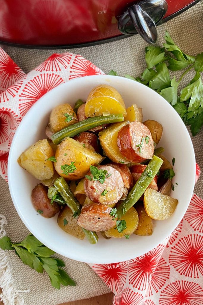 slow cooker sausage and potatoes with green beans in a white bowl on the table