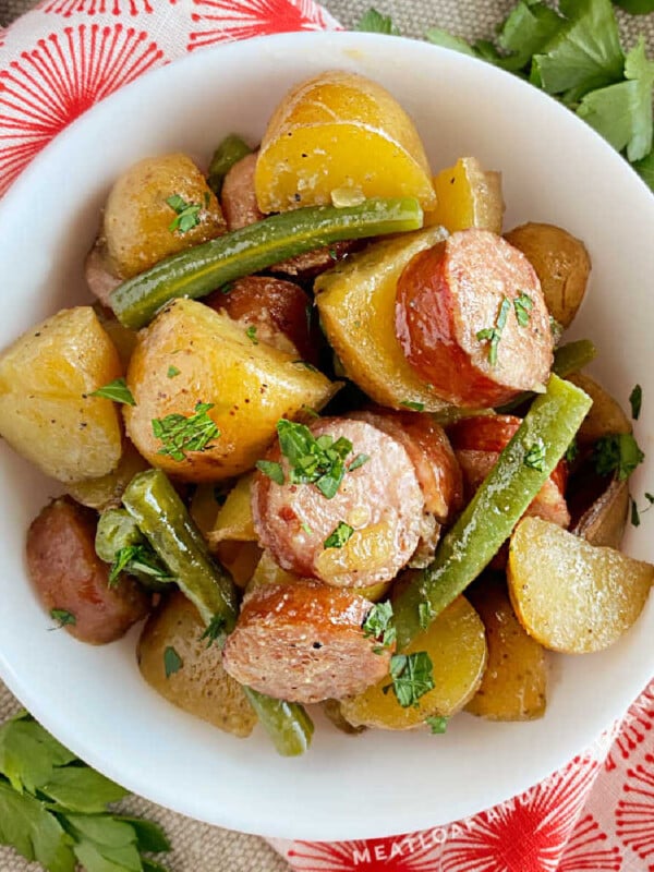 slow cooker sausage and potatoes with green beans in a white bowl