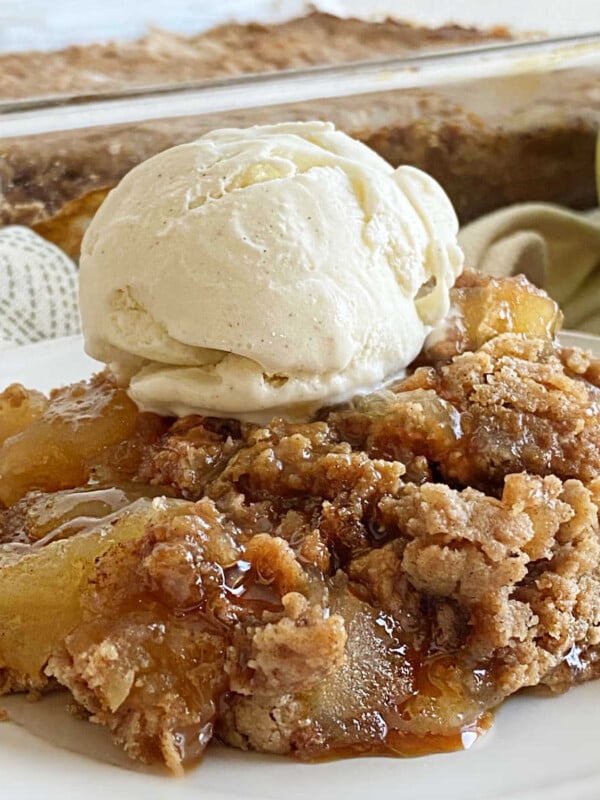apple pie dump cake with scoop of vanilla ice cream and caramel sauce on a plate