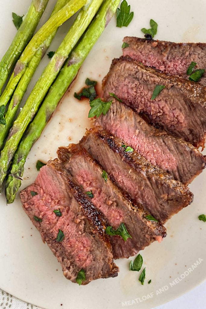 sliced new york strip steak cooked medium on ninja foodi grill xl with asparagus on plate