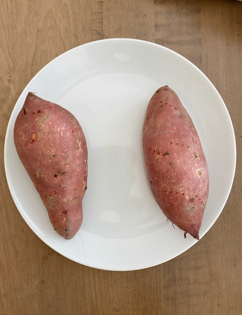 2 sweet potatoes with fork holes on a white plate