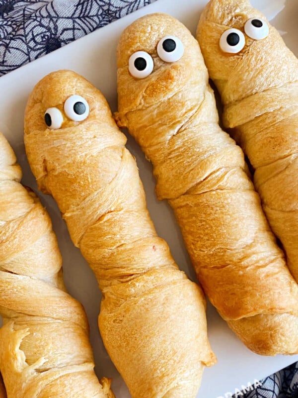 crescent mummy dogs for halloween with candy eyes on a white platter