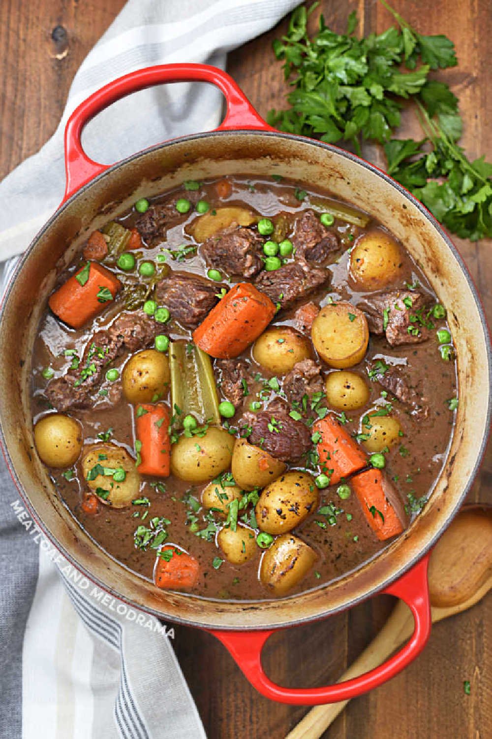 hearty beef stew in red le creuset dutch oven with carrots and baby potatoes