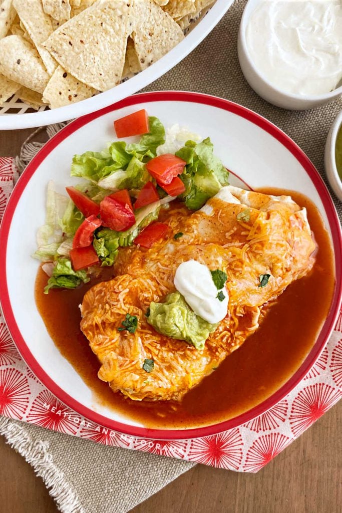 wet burrito enchilada style with red sauce on a plate with lettuce and tomatoes