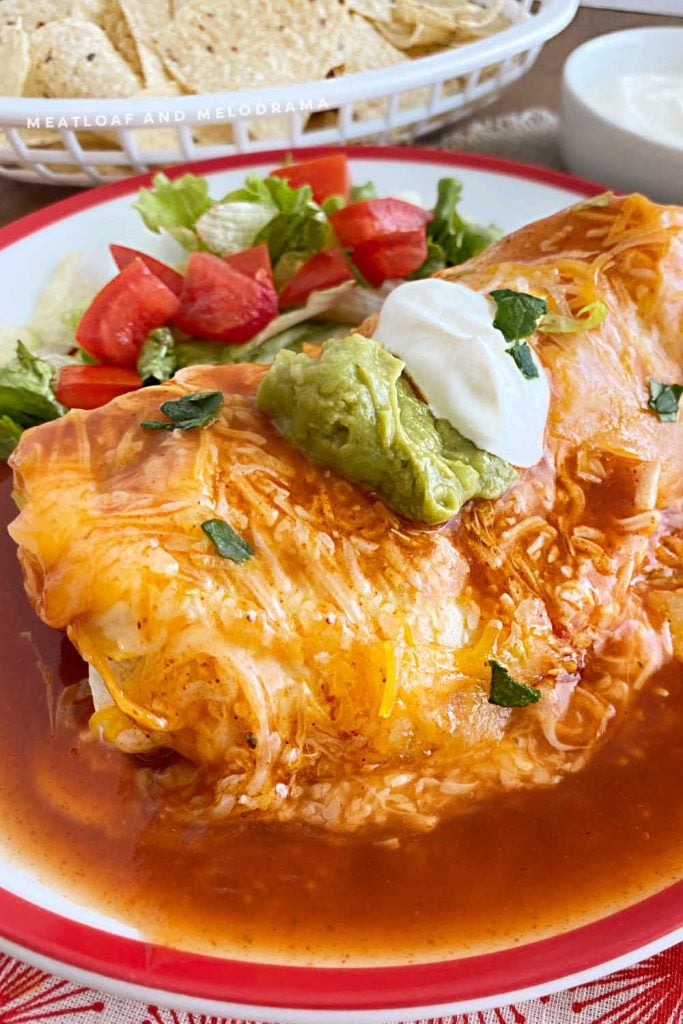 wet burrito smothered in red enchilada sauce and cheddar cheese on a plate