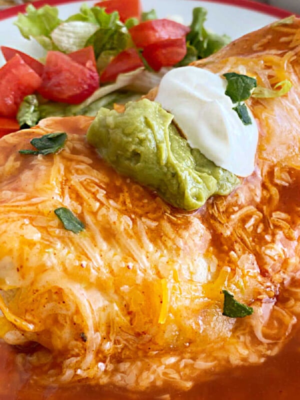 wet burrito smothered in red enchilada sauce and cheddar cheese with sour cream and guacamole