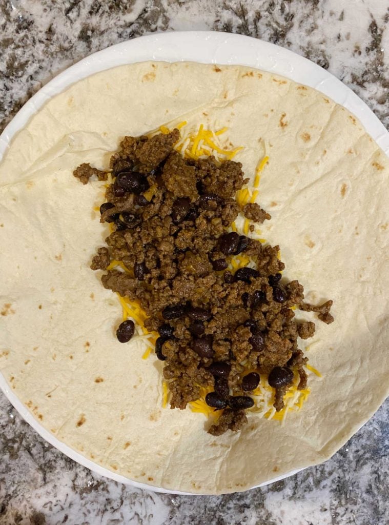 brown ground beef and black beans with shredded cheese in center of large tortilla