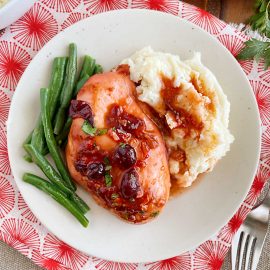 baked cranberry chicken with whole berries, green beans and mashed potatoes on plate