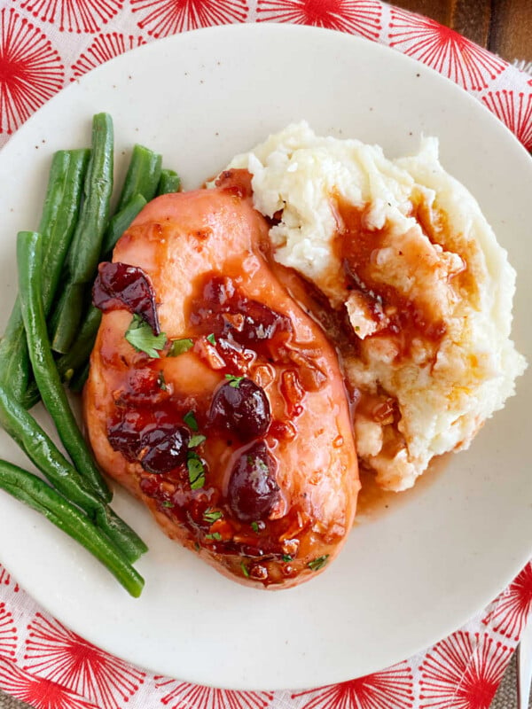 baked cranberry chicken with whole berries, green beans and mashed potatoes on plate