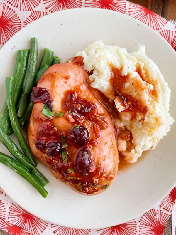 baked cranberry chicken with whole berries, green beans and mashed potatoes on plate