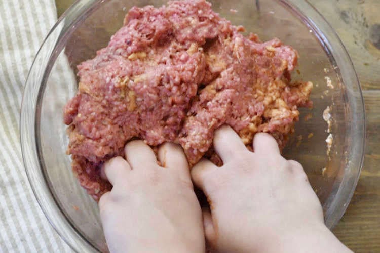 hands mixing meatball mixture in glass bowl