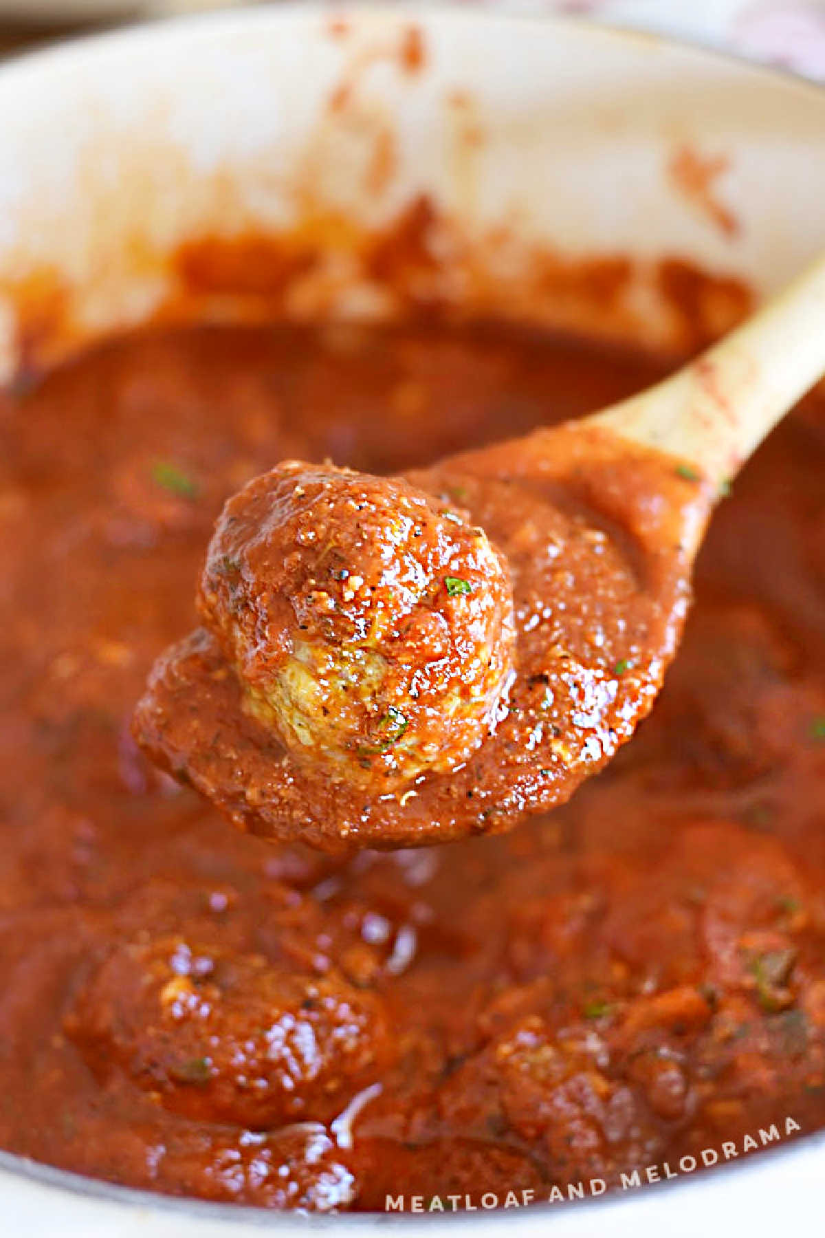 baked Italian meatball in marinara sauce on wooden spoon