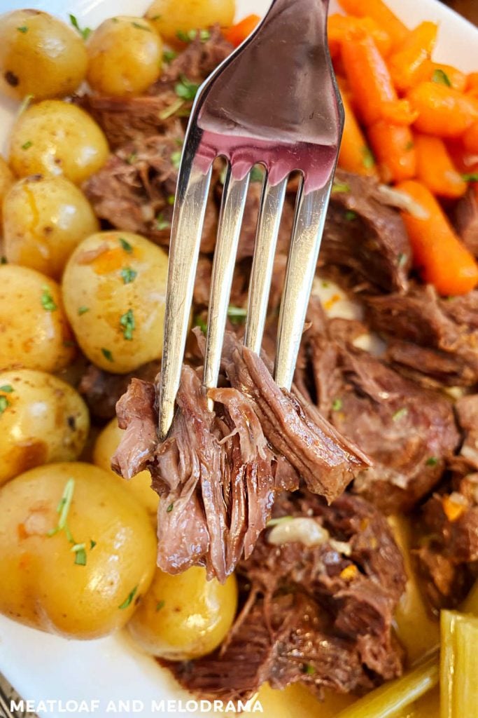 tender chuck roast on fork with baby potatoes and carrots on platter