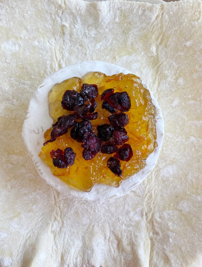 brie wheel on puff pastry topped with orange marmalade and dried cranberries
