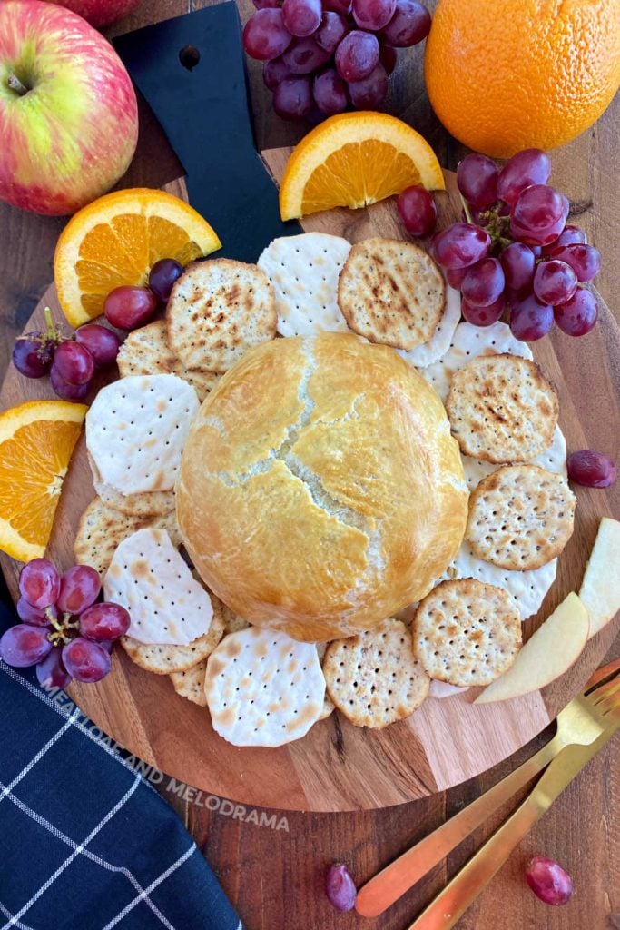 baked brie en croute puff pastry on bread board with fruit and crackers