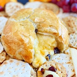 cut open baked brie with melted cheese, dried cranberries and crackers