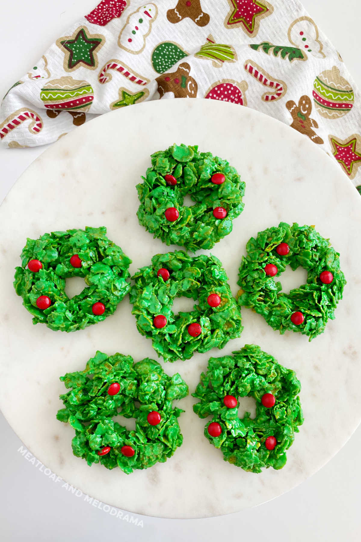 Christmas cornflake wreath cookies with red m & m candies on a marble cake stand