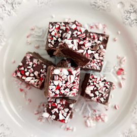 chocolate peppermint fudge with crushed candy canes on top on a white plate