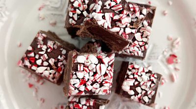 chocolate peppermint fudge with crushed candy canes on top on a white plate