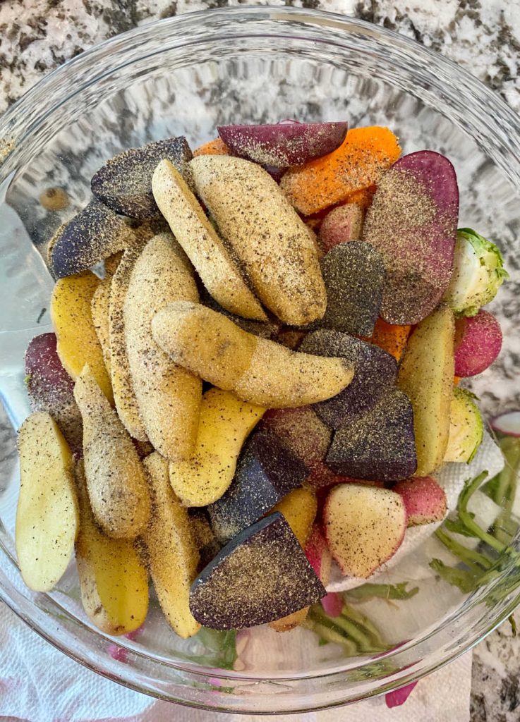 sliced root vegetables in mixing bowl with olive oil and seasonings