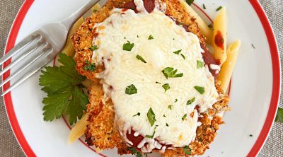 baked chicken Parmesan with penne pasta on a red and white plate