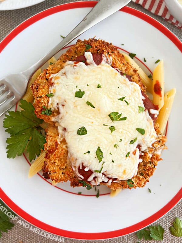 baked chicken Parmesan with penne pasta on a red and white plate